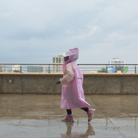 Girl wearing a pink raincoat walking on a rooftop with buildings in the background