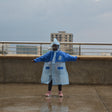 Person wearing a blue raincoat on a rooftop with buildings in the background