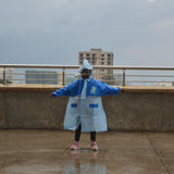 Person wearing a blue raincoat on a rooftop with buildings in the background