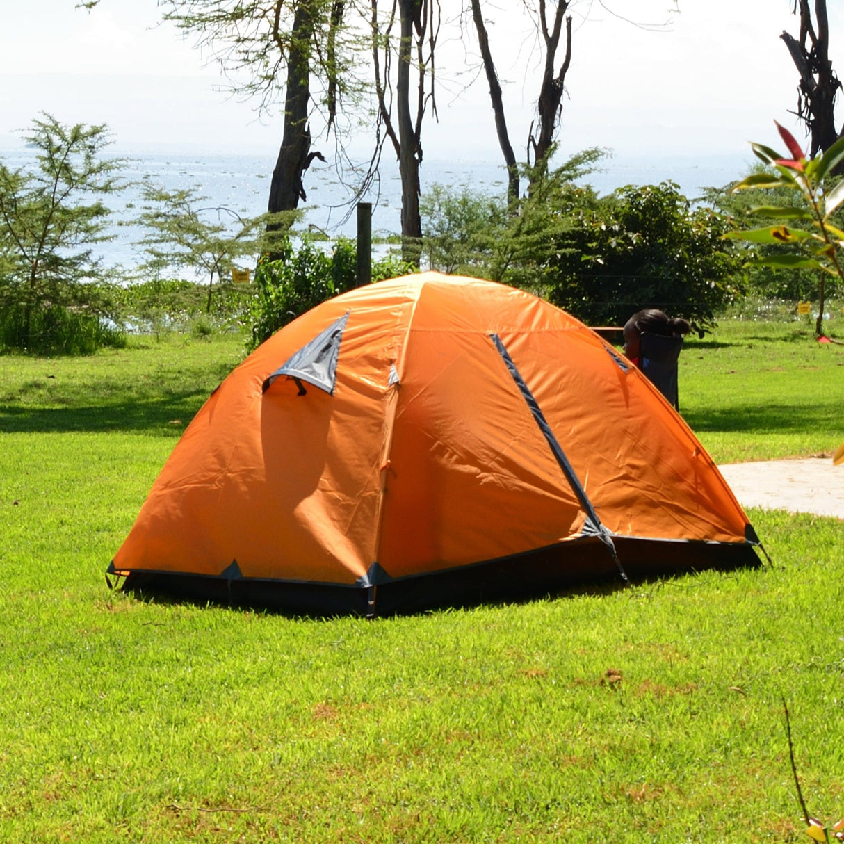 Orange tent on a grassy area with trees and a bench in the background